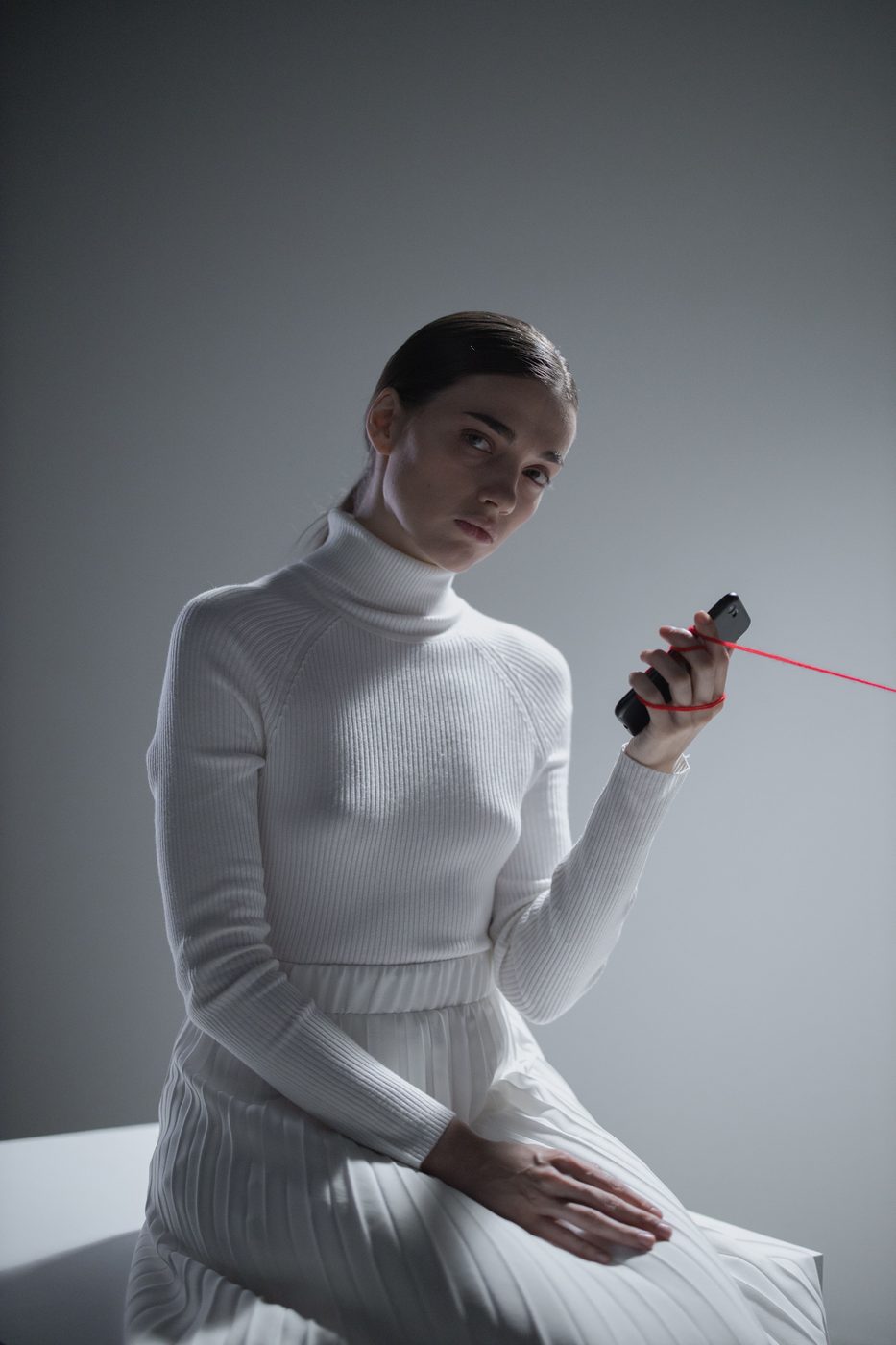 A woman looking away from a phone that is tied to her hand with red thread
